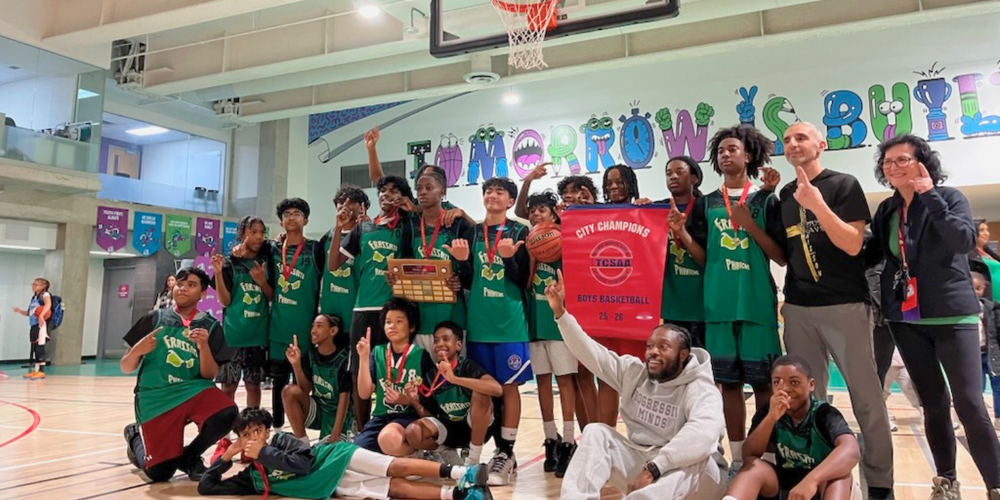 Basketball team posts with champions banner in a gym
