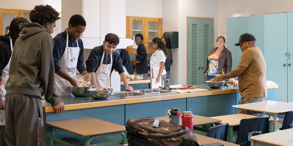 Photo of Chef Roger Mooking teaching Father Henry Carr students -prepare a balanced meal from scratch: saltfish buljol and roast bake