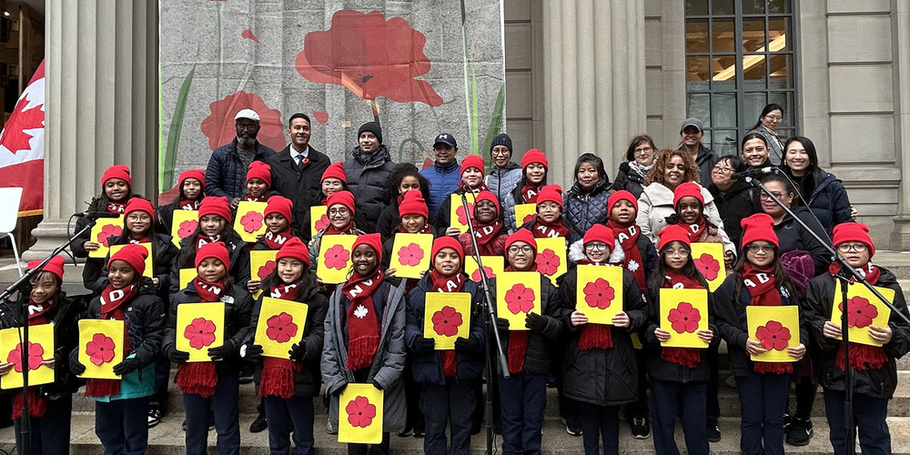 Group photo of Our Lady of Lourdes students with poppy props, along with TCDSB staff and Manulife personnel