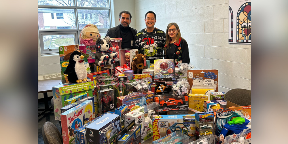 Three adults posing with a large pile of toys.