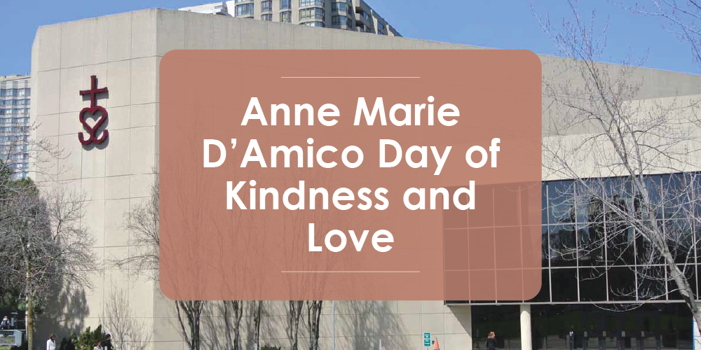 A photo of a modern school building with a cross mounted on the exterior wall, overlaid with a translucent panel reading “Anne Marie D’Amico Day of Kindness and Love.” Trees and nearby buildings are visible in the background.