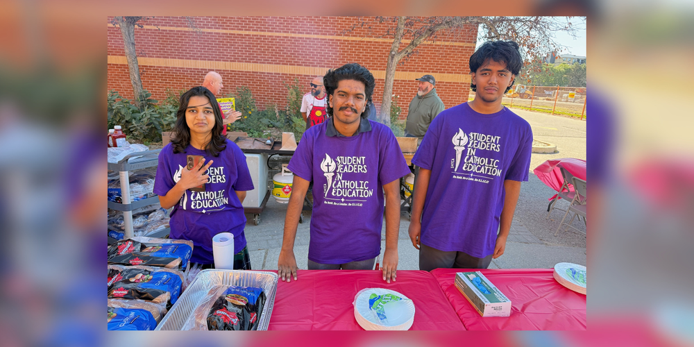 3 students in purple shirts behind a table
