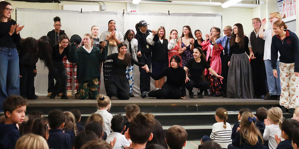 Group photo of Notre Dame theatre players bowing on stage while St. John students watch and clap from the audience