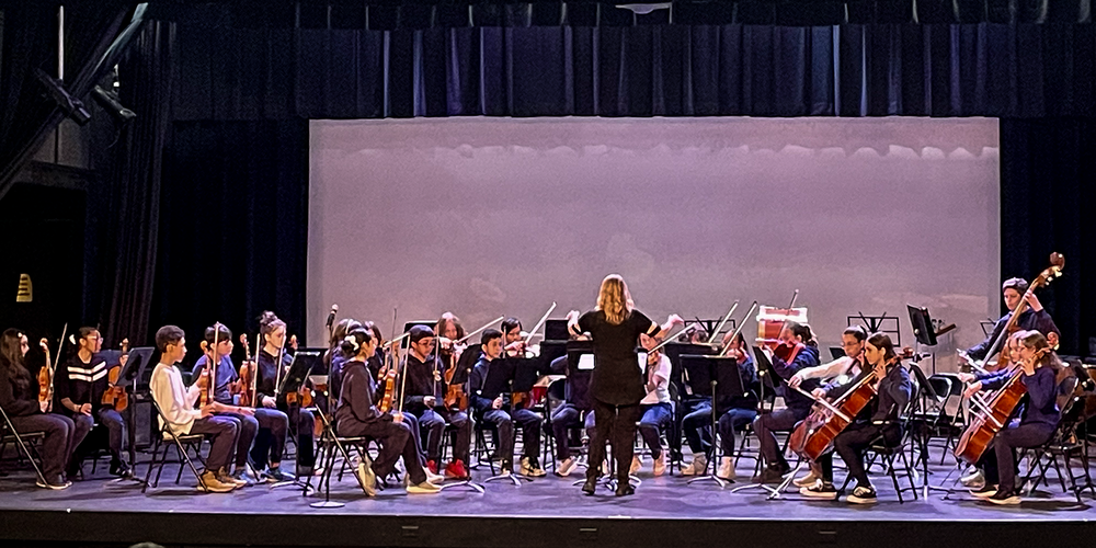 Photo of teacher conducting TCDSB music students on the stage