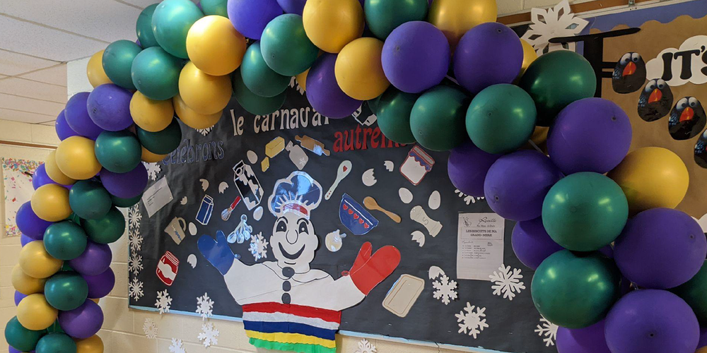 A classroom board decorated with a paper bonhomme and paper snowflakes and other graphics around a balloon arch for Carnaval