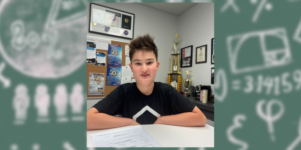 A student sitting at a desk with awards behind him. 