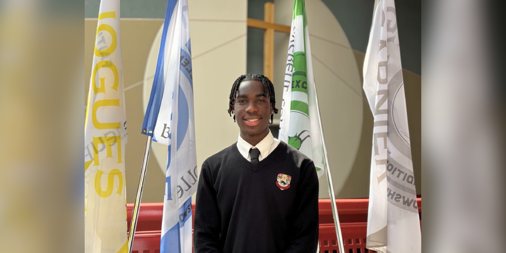 Student posing in uniform in front of 4 flags.