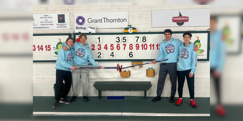 4 students posing with curling equipment in front of a score board.