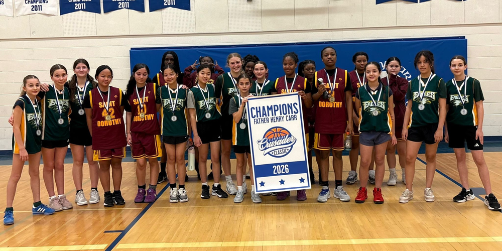 A girls basketball team photo in the gym, holding up a Champions 2026 banner