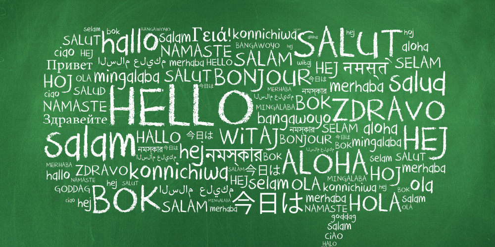 Green chalkboard-style background featuring the word “HELLO” in large white letters at the center, surrounded by smaller “hello” greetings in many languages.