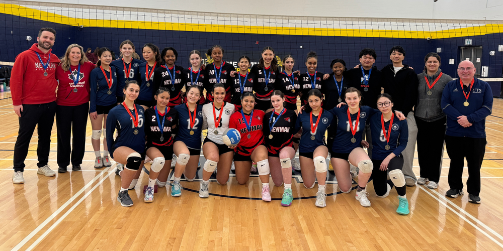 A volleyball team posing in a gym with medals around their necks.