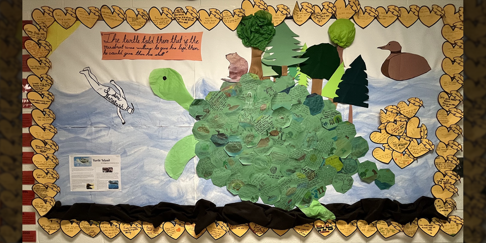 Photo of art display created by St. Angela students, which shows a land turtle, along with a person and a duck swimming in the sea around the turtle, along with explanatory text