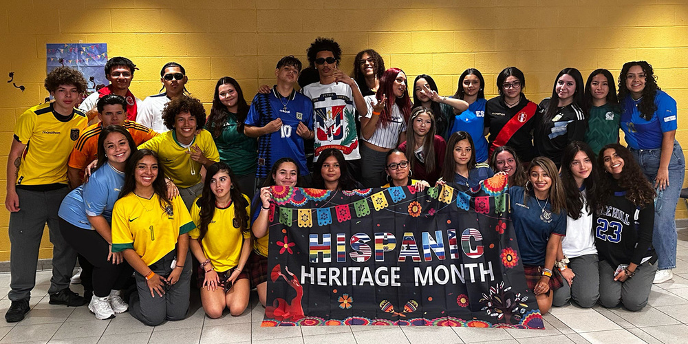 Group photo of St. Basil-the-Great College School's Hispanic Student Association with a Hispanic Heritage Month flag showing the flags of various Hispanic countries and cultural graphic elements