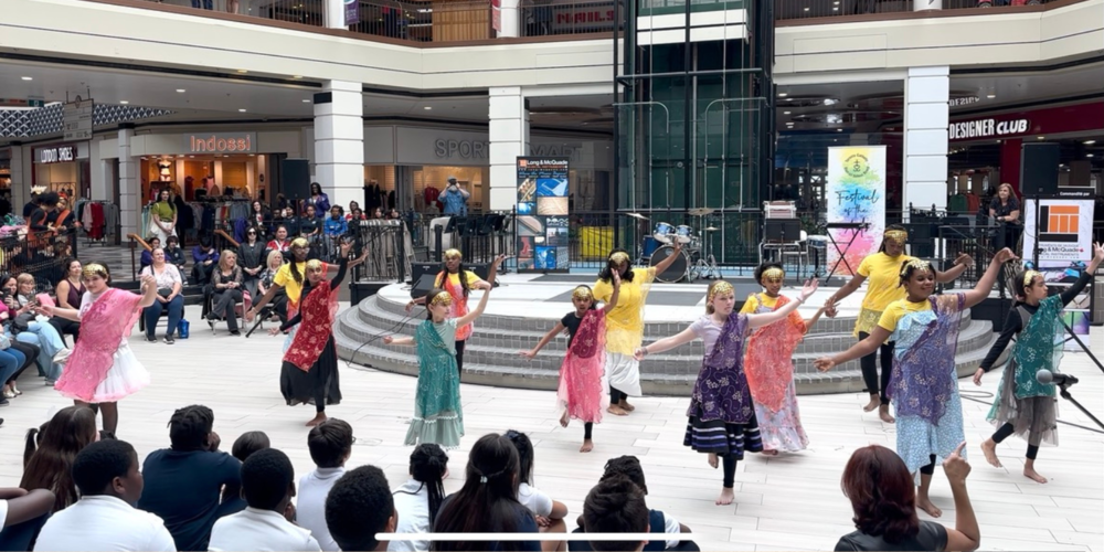 A group of children dancing in the middle of a mall area, wearing cultural garb
