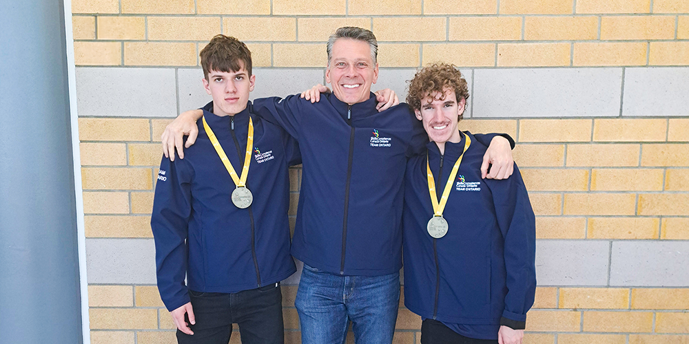 Photo of Owen R. and Alexander C. with their medals posing with their coach