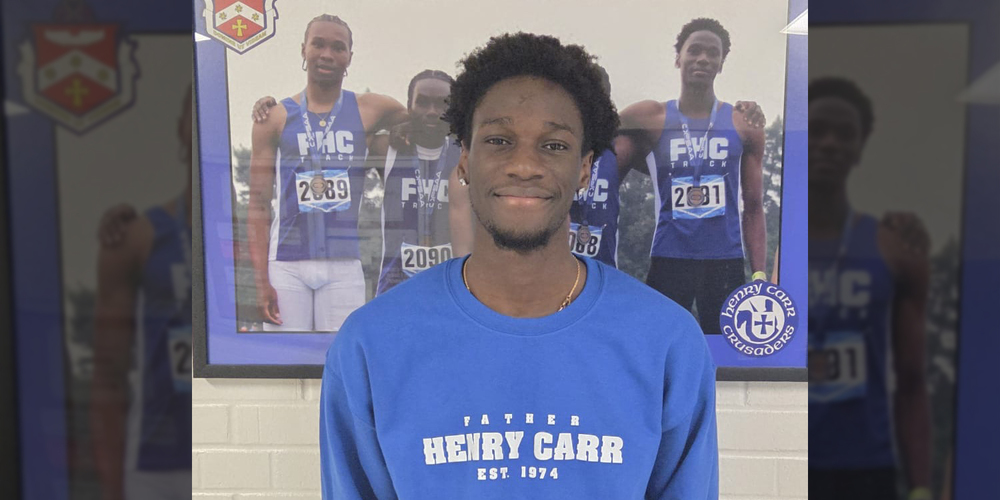 Photo of Adnan standing in a FHC sweater in front of a framed photo that shows his medalling performance