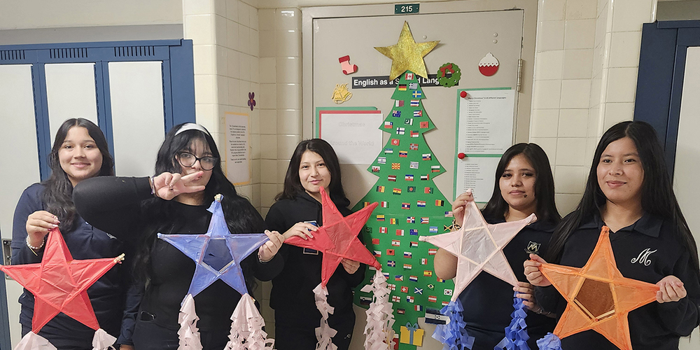 Photo of students holding up the Parols they made in front of a Christmas tree display