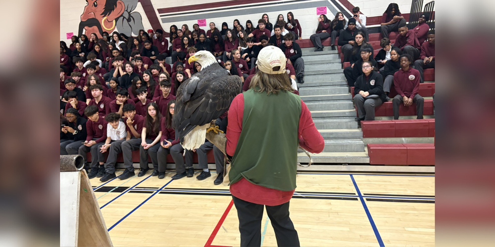 A woman holding an eagle in front of a large group of students in a gym. 