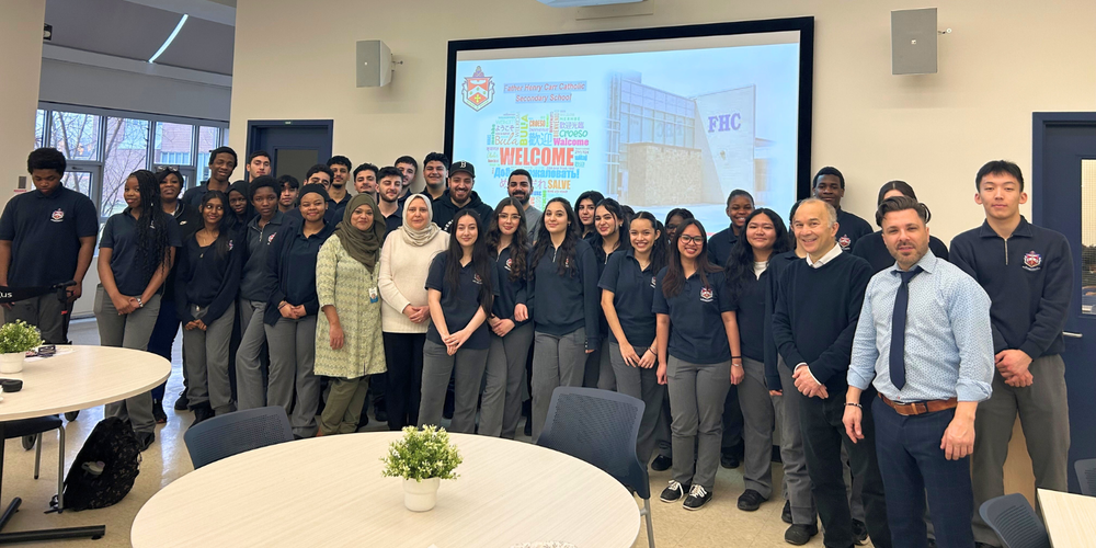 Large group of students and adults in front of a projector that reads "Welcome"