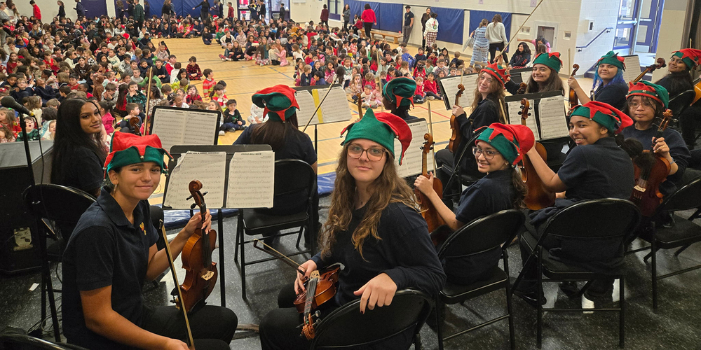 Photo of MPJ Strings students with their instruments and Christmas hats, ready to perform to the elementary students