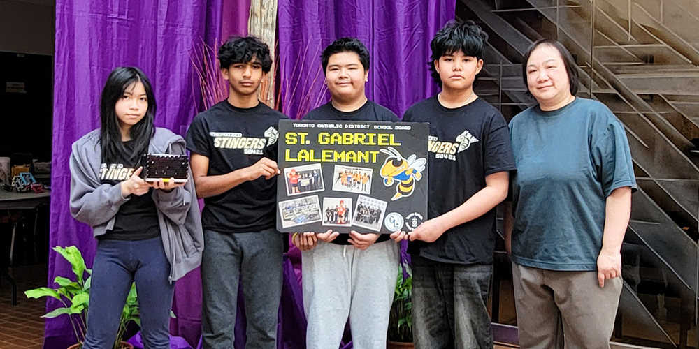 Photo of St. Gabriel Lalemant students holding up their robot and poster board