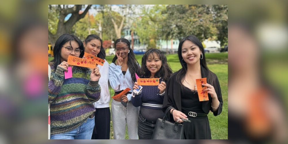 5 girls posing with orange cards that read "Newman"