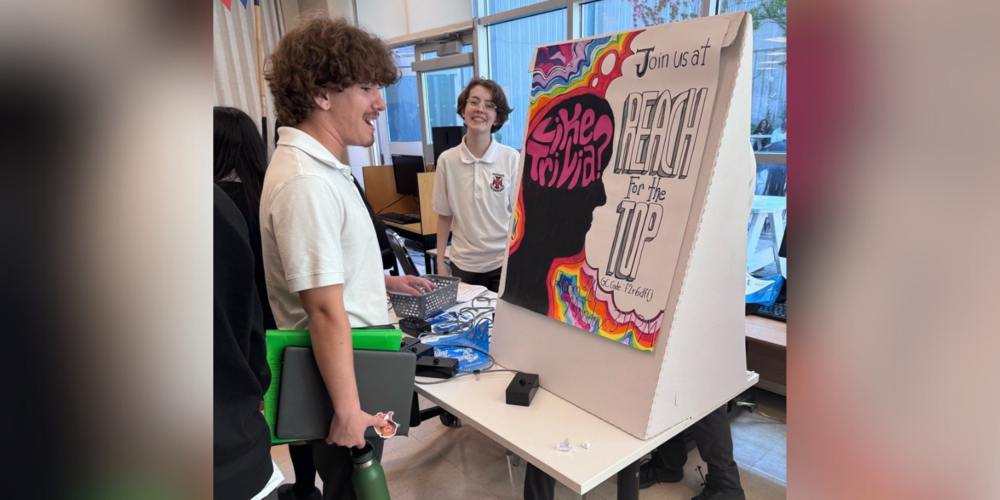 2 students looking at a poster board that says "Like trivia? Join us at Reach for the Top"