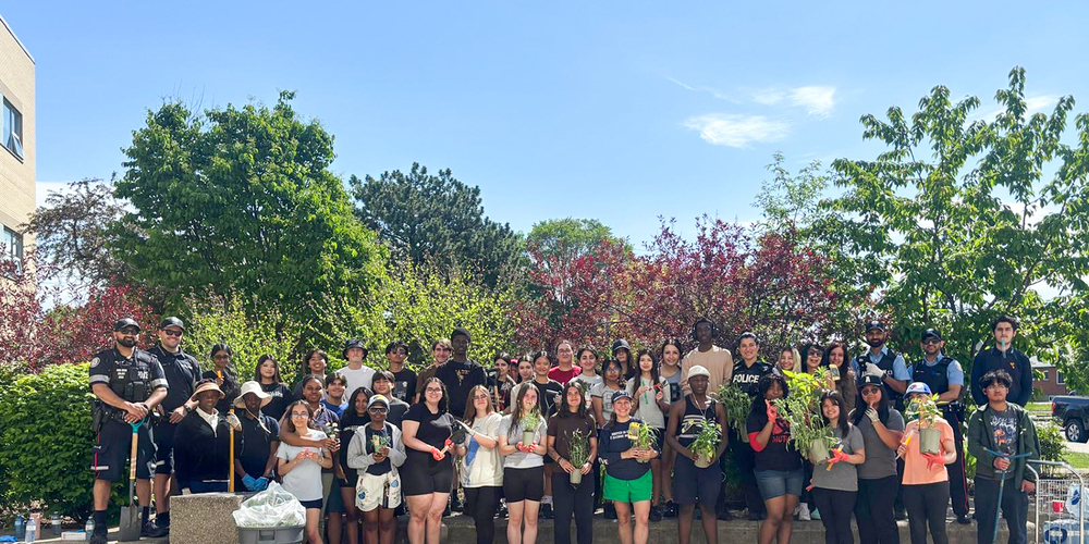 Group photo of MPJ students and staff and helpers holding plants from the garden and gardening equipment