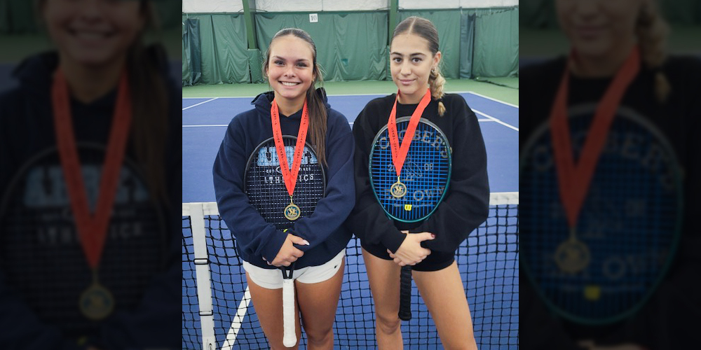 Photo of Juliana and Sophia on the court with their tennis rackets wearing their championship medals