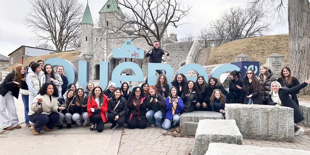 Photo of SJCS students and staff in front of blue Quebec sign