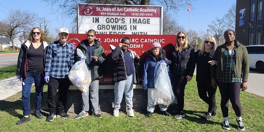 Group photo of SJOA students and staff with the garbage they cleaned up, posting in front of the school name sign