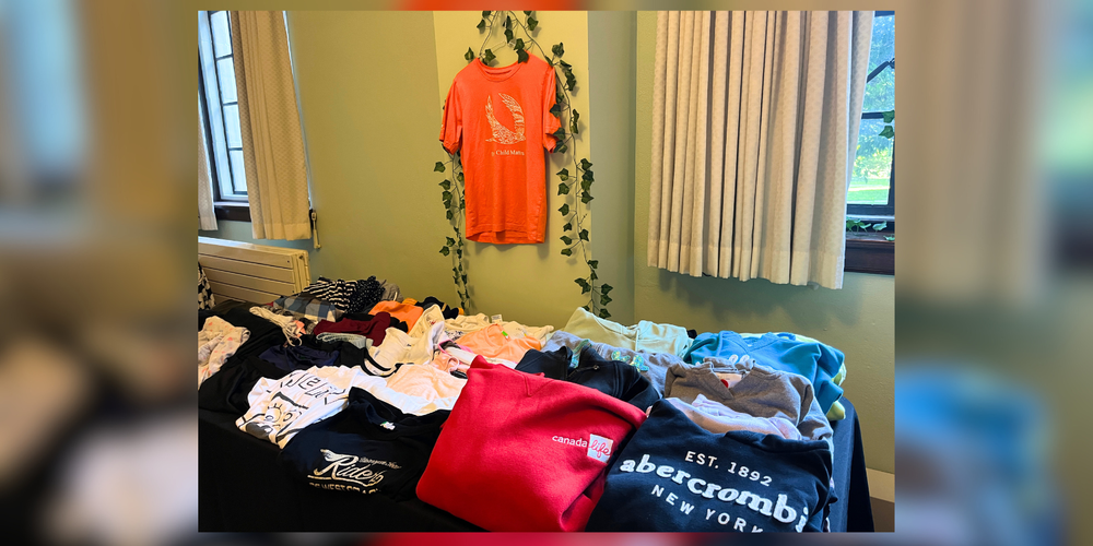 Clothes folded on a table, and an orange shirt hanging on the wall.