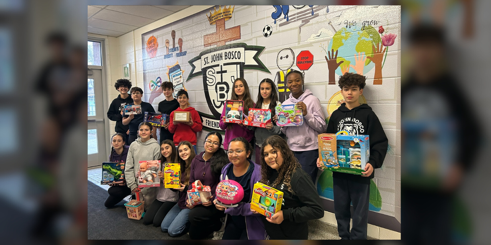 A group of students posing with toys in front of St. John Bosco mural