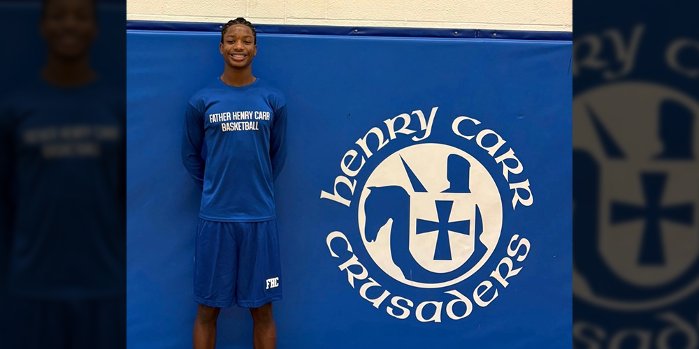 Photo of Smith in basketball uniform in from of a board that has the Henry Carr Crusaders logo on it
