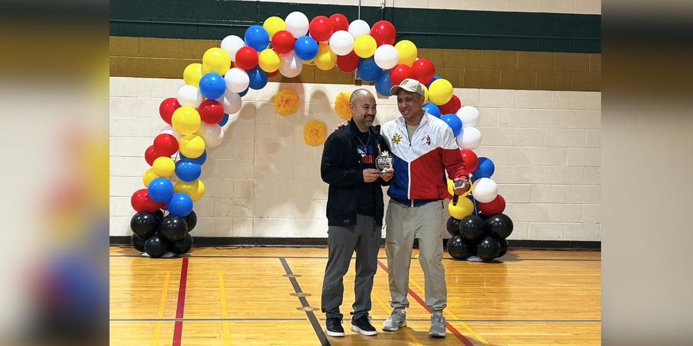 Two adults posing in front of a balloon arch.