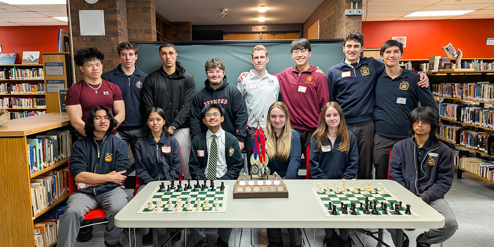 Photo of students at the tournament posing together with chess boards and awards