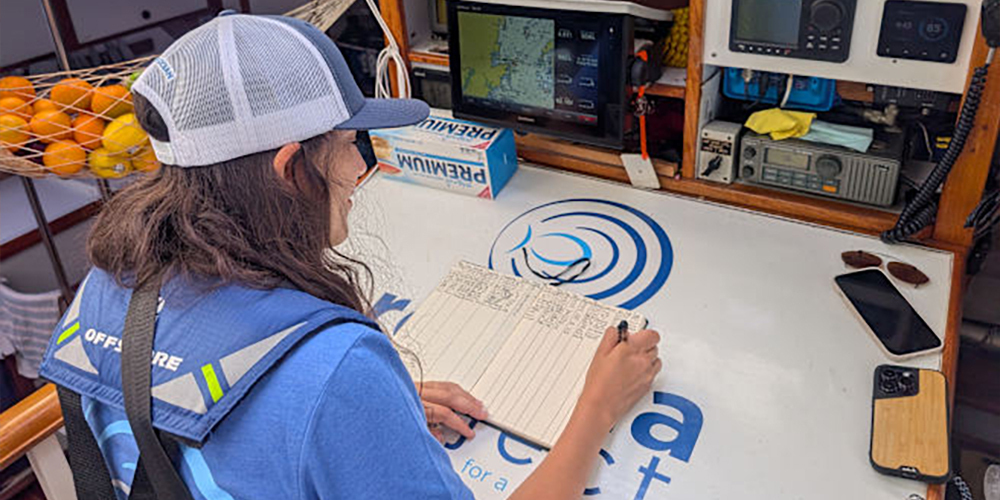 Photo of Sarah Gallah aboard Rozalia Project's American Promise vessel, collecting data from the navigation station for her microplastics datasheet.
