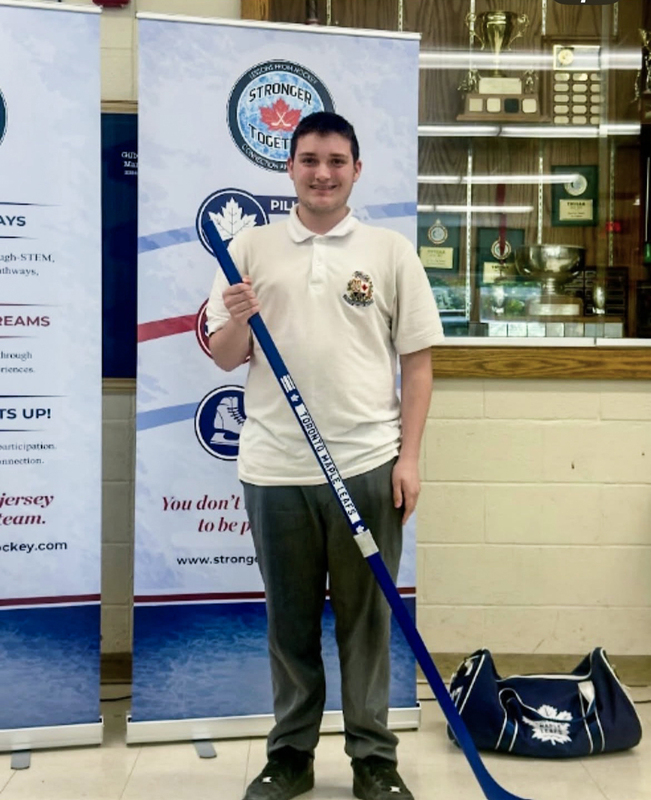 Photo of a Chaminade student holding up a new hockey stick with a new hockey bag in the background