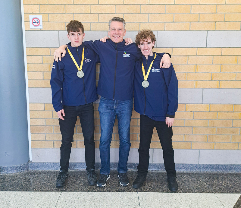 Photo of Owen R. and Alexander C. with their medals posing with their coach