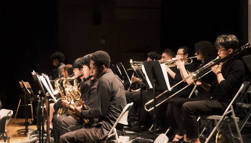 Photo of music students giving a performance while being conducted by their teacher