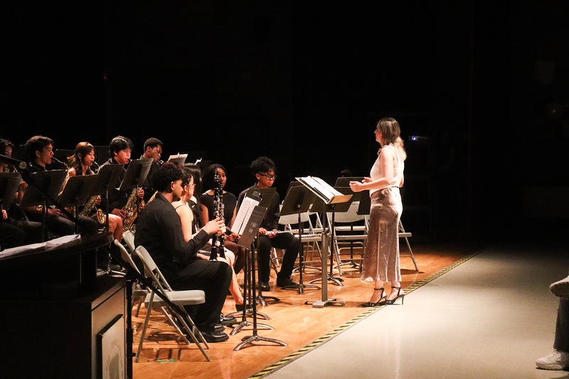 Photo of music students giving a performance while being conducted by their teacher