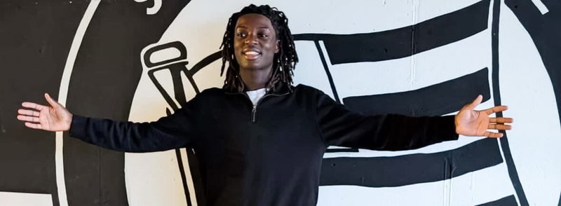 Photo of Elijah raising his arms in front of Austrian Soccer Club SK Sturm Graz team logo banner