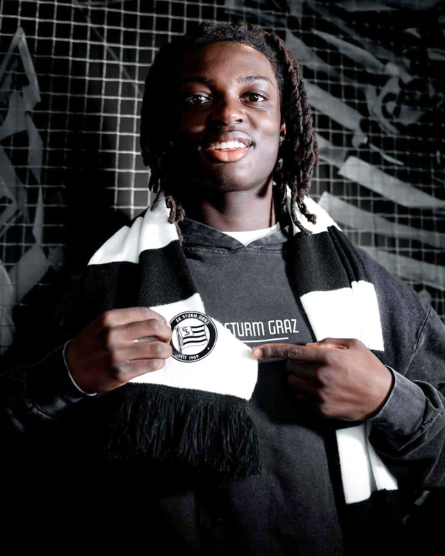 Photo of Elijah wearing a Austrian Soccer Club SK Sturm Graz team scarf and pointing to the club logo on the scarf