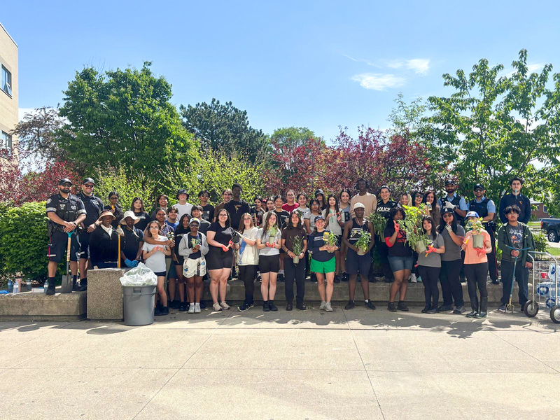 Group photo of MPJ students and staff and helpers holding plants from the garden and gardening equipment