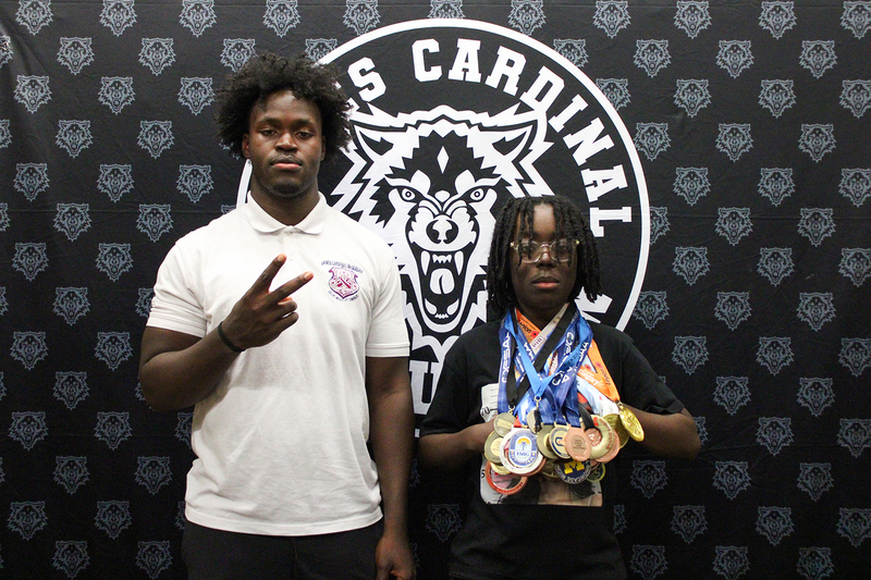 Eghosa at the signing with his sibling who is posing with all of Eghosa's medals at once