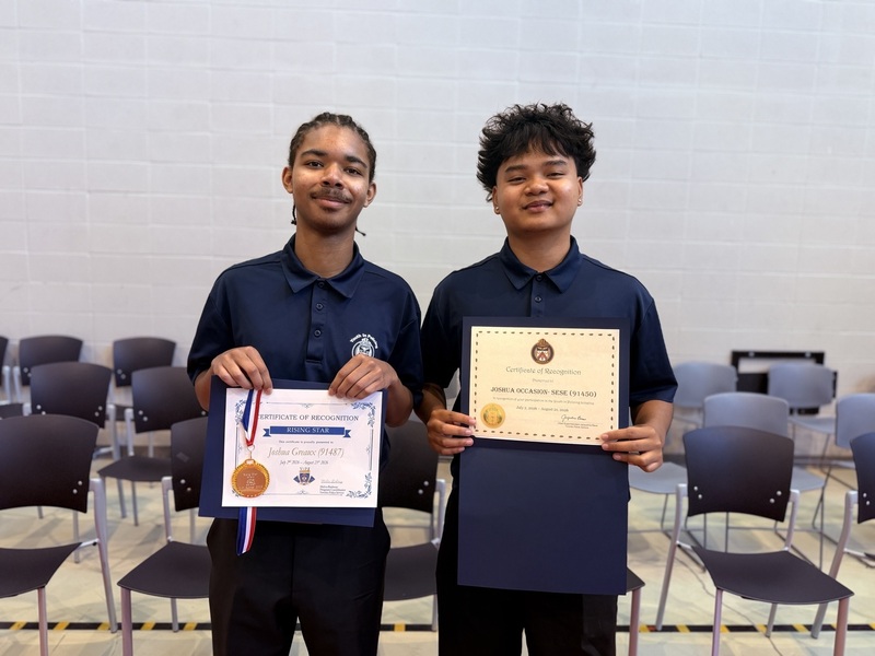 Two students pose indoors while holding certificates of recognition and wearing medals from the Youth in Policing Initiative program.