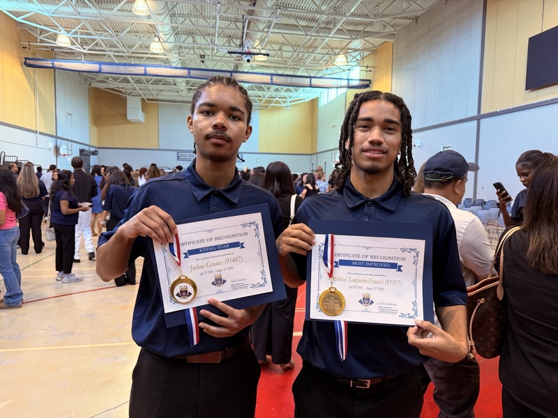 Two students pose indoors while holding certificates of recognition and wearing medals from the Youth in Policing Initiative program.