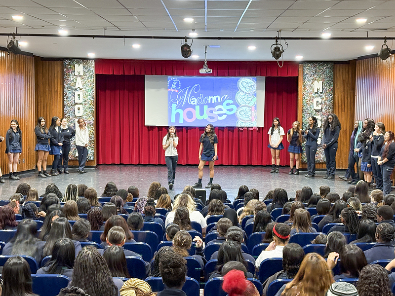 Photo of the organizing students speaking to the other Madonna students about the new House system, with a presentation on the projector screen behind them