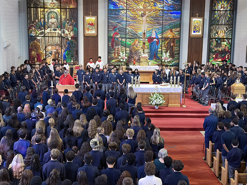 Redmond students and staff attend the Mass in the church, facing the spakers with huge sweeping religious stained glass mural artwork beyond the speakers