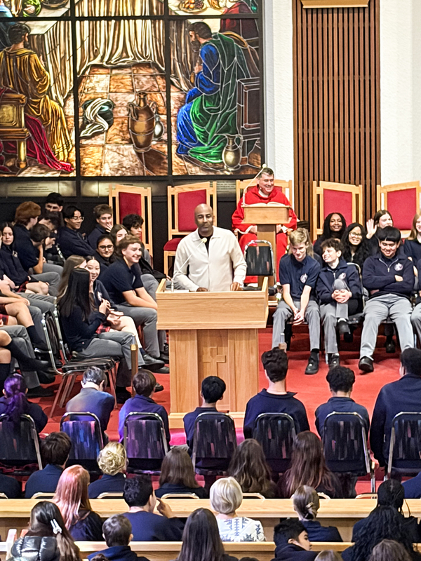Redmond students and staff attend the Mass in the church, facing the spakers with huge sweeping religious stained glass mural artwork beyond the speakers